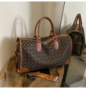 Detail der großen braunen Reisetasche mit Rautenmuster, Ledergriffen und Gurt