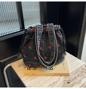 Detail view of denim bucket bag with cherry embroidery and frayed denim edges