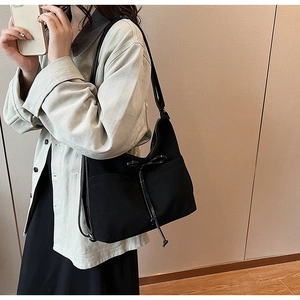 Detail of black tote bag with drawstring bow and side pocket shown on shoulder