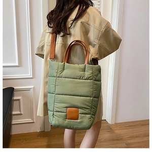 Detailed view of light green quilted tote bag with brown leather handles on shoulder