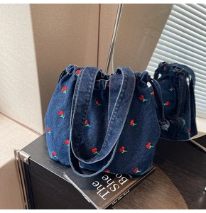 Detail of deep blue denim bucket bag with red and green cherry embroidery and drawstring