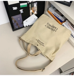 Detail of adjustable strap and metal buckle on cream canvas crossbody bag with text