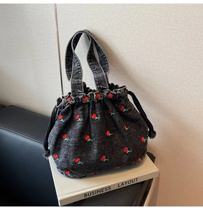 Close-up of red cherry embroidery patterns on dark grey washed denim bucket bag