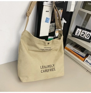 Close-up of beige canvas crossbody bag with Leisurely text in a cozy home setting