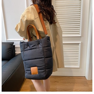 Detail of black quilted down bucket bag with brown leather handles on a model