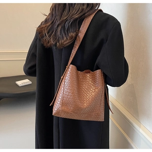 Détail d'un sac seau marron avec relief crocodile et texture tissée porté par un mannequin