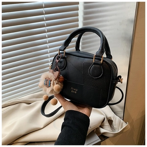 Detail of black lychee leather crossbody bag with golden logo and plush bear charm