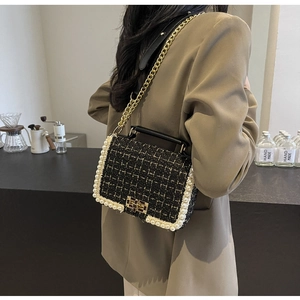 Detail of tweed crossbody bag with pearl trim and gold chain strap on female model