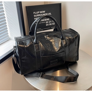 Detalle de bolsa de viaje en cuero negro brillante con correa ajustable y logo metálico