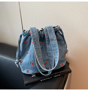 Detail of blue denim bucket bag featuring vibrant red cherry embroidery and drawstring