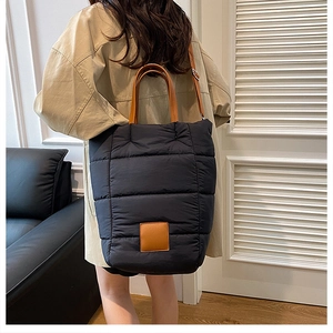 Detail of black quilted puffer tote bag with brown leather handles and shoulder straps