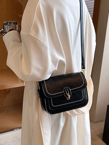 Petit sac carré noir avec broderies blanches et boucle dorée porté par un modèle