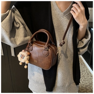 Brown leather Boston bag with geometric pattern and cute lion charm held by a model