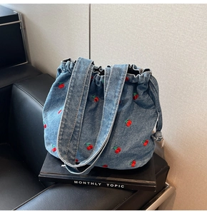 Detailed close-up of embroidered cherry patterns on blue denim bucket bag surface