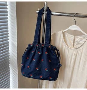 Close-up of deep blue denim bucket bag featuring vibrant red cherry embroidery details