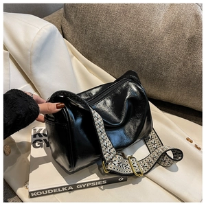 Detail of glossy black cylinder bag with wide geometric jacquard strap on white blazer