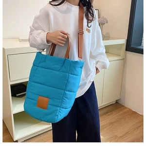 Blue quilted bucket bag with brown handles worn by a model in a modern home setting