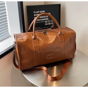 Detalle de bolsa de viaje de cuero marrón con logo NOCO, asas dobles y cremalleras metálicas