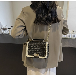 Detail of tweed crossbody bag with white pearls and gold chain on model in cafe