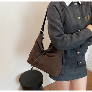 Detail of dark brown suede shoulder bag featuring an elegant leather bow decoration