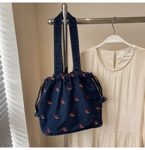 Detail of dark blue denim bucket bag featuring vibrant red cherry embroidery patterns