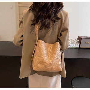 Détail d'un sac seau en cuir tressé marron avec large bandoulière sur l'épaule