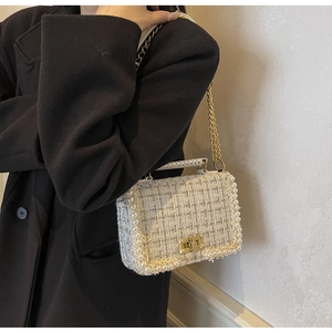 Detailed close-up of tweed shoulder bag with faux pearl trim and golden chain strap