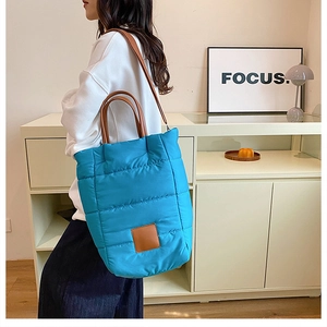 Detail of blue quilted bucket bag featuring brown leather handles and a focal logo patch
