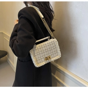 Detailed view of tweed crossbody bag with pearl trim and gold chain strap on a black blazer