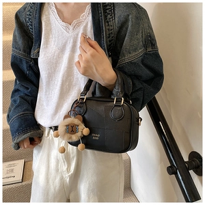 Detail of black leather crossbody bag featuring geometric panels and lion charm pendant