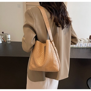 Détail de la texture tressée du sac seau kaki porté par un mannequin dans un café