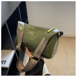 Detail of dark green pillow bag showing oil-wax leather texture and wide woven strap