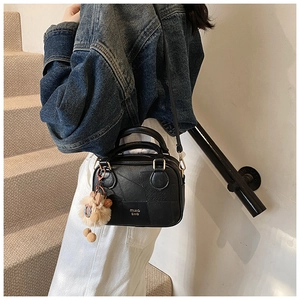 Detail of black crossbody bag with litchi texture and cute plush animal charm accessory
