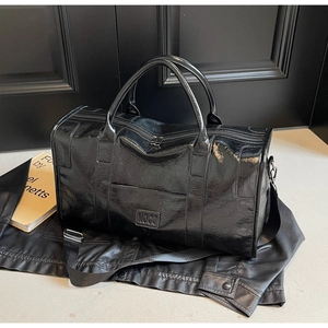 Primer plano de bolsa de viaje en cuero negro brillante con logo NOCO y correa ajustable