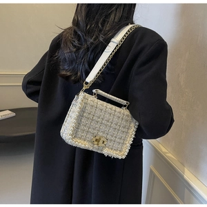 Detail of tweed crossbody bag with pearl trim and gold hardware on a black coat