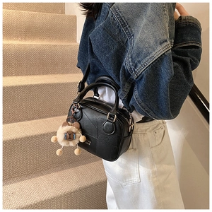 Close-up of black leather mini Boston bag with textured panels and plush toy charm