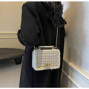 Detail of tweed crossbody bag with pearl trim, gold chain strap, and metallic lock closure