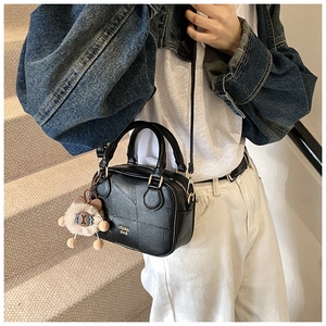 Detail of black crossbody bag with logo and cute brown teddy bear plush charm