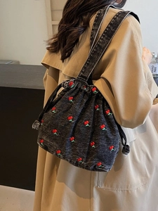 Denim drawstring bucket bag with red cherry embroidery shown on model shoulder