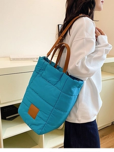 Blue quilted puffer bucket bag with brown leather straps worn by a model in a room