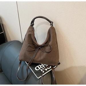 Detail of brown suede tote with leather bow accent and metal zipper on grey seat