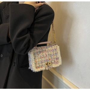 Detail of colorful tweed handbag with pearl trim and gold chain on a black coat