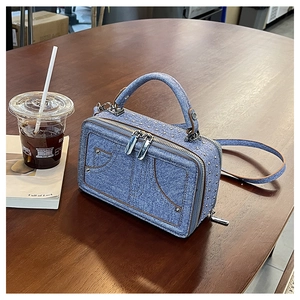 Detail der hellblauen Denim-Tasche mit silbernen Nieten auf einer Holzoberfläche