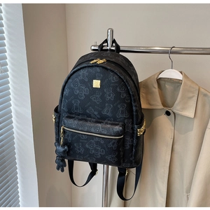Detail eines schwarzen Rucksacks mit Bärenmuster, goldener Plakette und seitlichen Nieten