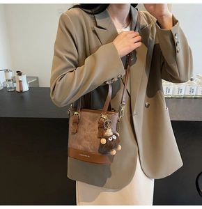 Detail of coffee brown bucket bag with plush bear charm worn with a stylish blazer