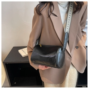 Detail of black cylinder bag featuring a trendy wide woven strap and gold zipper hardware