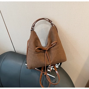 Detail of a brown suede tote bag with a decorative drawstring bow and silver hardware