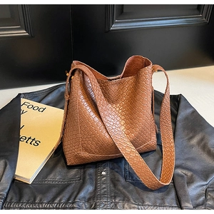 Détail d'un sac bandoulière en cuir tressé marron sur une veste en cuir noir