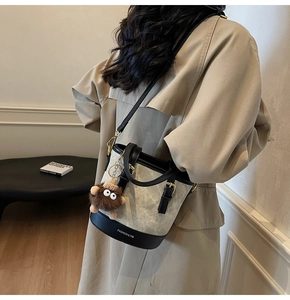 Detail of beige canvas bucket bag with black leather trim and plush monkey charm
