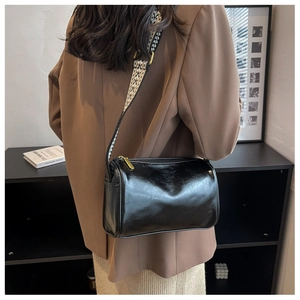 Detailed view of black cylinder bag with geometric jacquard strap worn by a model